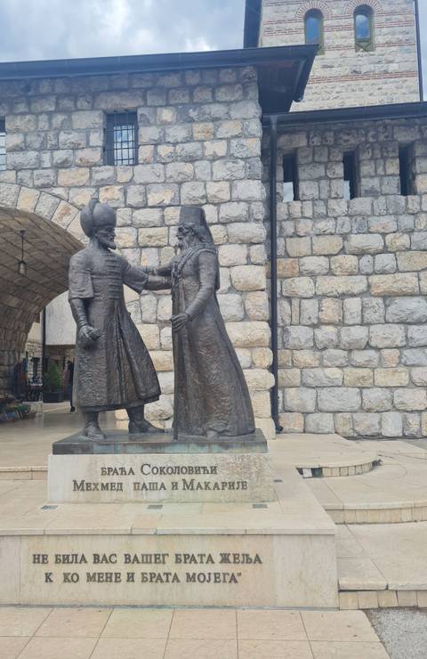 Life-size bronze statues in Ottoman attire greet each other within a stone courtyard passage.