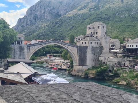 Iconic stone Stari Most bridge arcs over the emerald Neretva River as visitors watch kayakers below.
