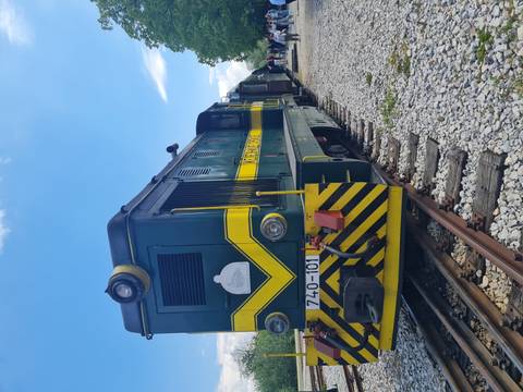 Green and yellow diesel locomotive on narrow-gauge tracks under blue sky at a heritage railway.