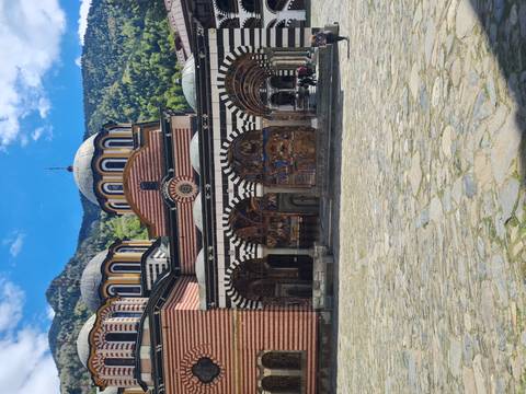 Colorful striped arches and domes of Rila Monastery courtyard surrounded by forested mountains.