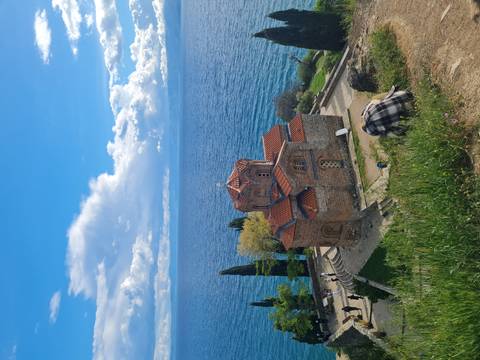 Stone Church of St John Kaneo perched on a cliff above Lake Ohrid with visitors on paths below.