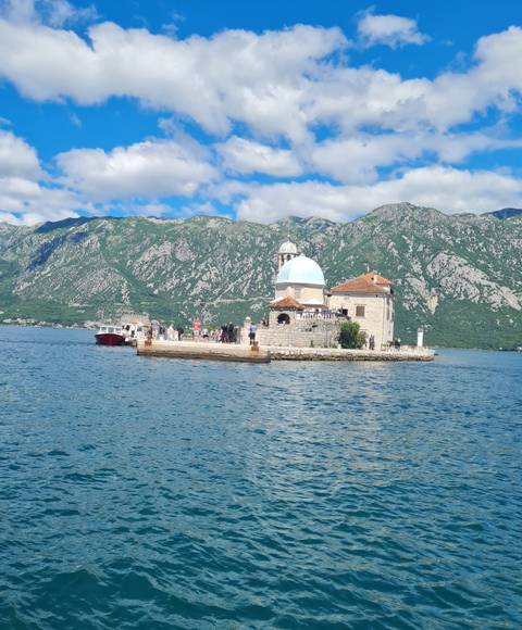 Boats dock beside tiny Our Lady of the Rocks church on a man-made island set against the green mountains of the Bay of Kotor.