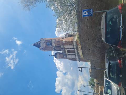 Brick Gardoš Tower rises above a stone wall and parked cars under a partly cloudy sky.