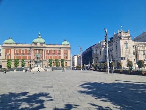 Expansive Belgrade Republic Square with National Museum, Prince Mihailo equestrian monument and surrounding historic buildings under a clear blue sky.