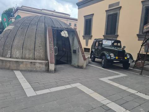 Small domed museum entrance beside a vintage military jeep on a cobbled street.