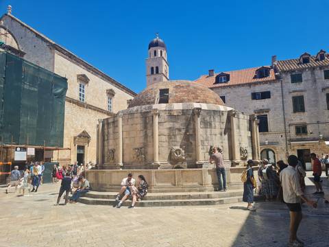 Sun-lit plaza with Onofrio’s Fountain and surrounding stone buildings in Dubrovnik’s Old Town.