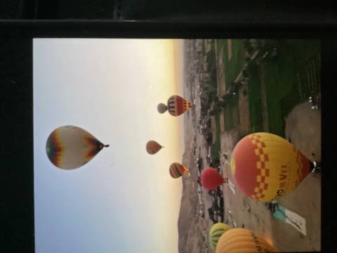 Colorful hot-air balloons drift over fields and desert terrain at sunrise in Luxor.