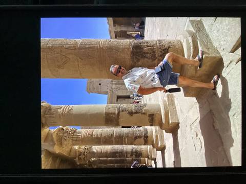 Tourist leans playfully against carved sandstone columns in Philae Temple.