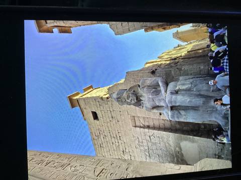 Massive seated statue of Ramses II towers above visitors inside Karnak Temple complex.