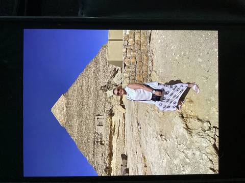 Woman stands smiling in front of a towering pyramid under a deep blue sky.