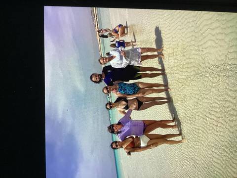 Friends in swimwear stand in shallow turquoise water on a sunny beach.