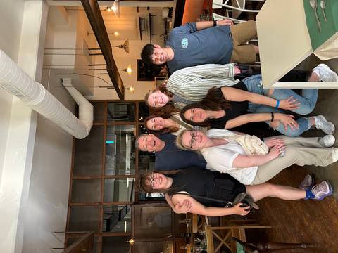 Indoor group photo of travellers posing with a smiling chef inside a modern restaurant.