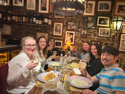 Group of six enjoying pasta and wine inside a cosy brick-walled Italian trattoria lined with photos.