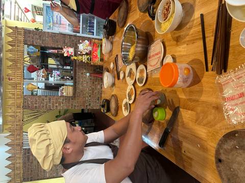 Chef in a cooking class arranges spices and ingredients on a wooden table under warm light.