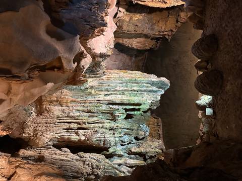 Illuminated stalactites and rock formations inside a large cave chamber.