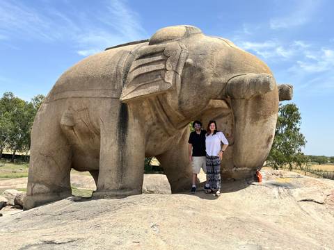 Couple poses beneath a massive ancient elephant rock carving under a clear blue sky.