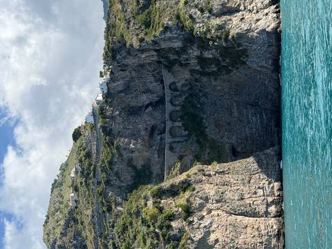 Steep rocky cliff with arched coastal road above turquoise Mediterranean water