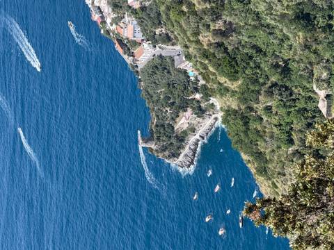 High aerial view of a coastal tower and village perched above deep blue sea with boat wakes