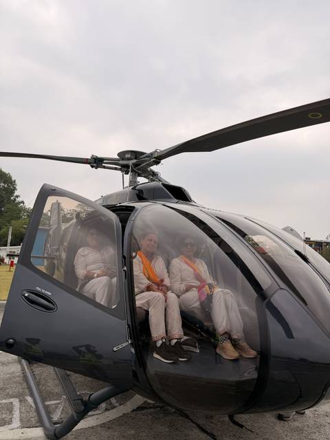 Three passengers dressed in white sit inside a sleek helicopter on a landing pad ready for takeoff.