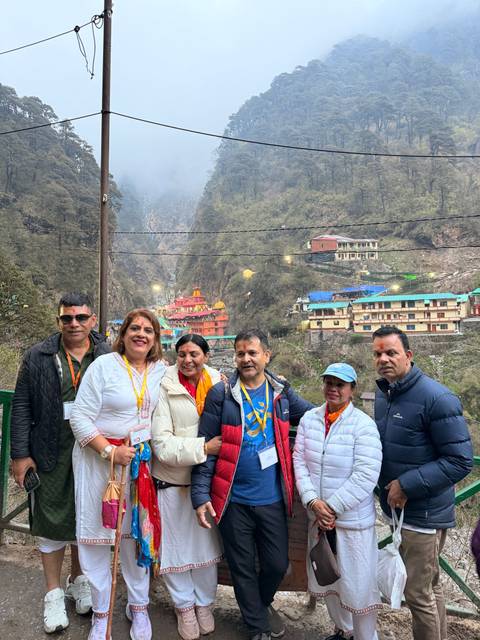 A tour group poses in front of colorful hillside temples and lodges nestled in a misty Himalayan valley.