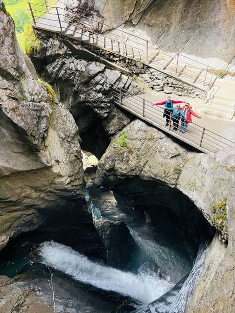 Travelers spread arms on a walkway above a deep rocky gorge with rushing water below