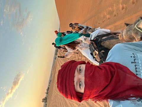 Selfie from camelback capturing fellow riders along golden sand ridges in the soft dawn light.