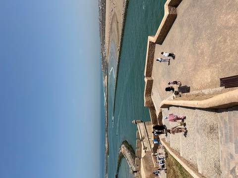 Panoramic view from ramparts over a turquoise river mouth and Atlantic coastline with visitors exploring the fort.