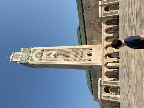 Visitor admires the soaring Hassan II Mosque minaret framed by elegant arches under a flawless sky.