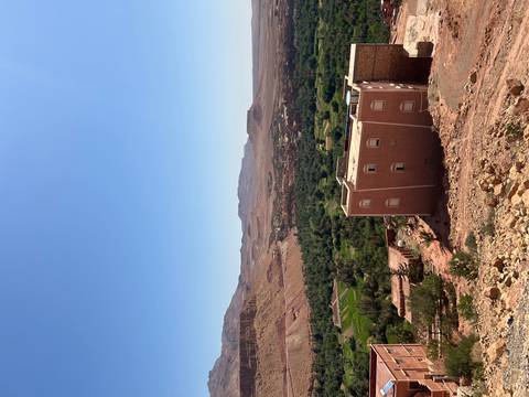Arid mountain valley with patchwork green oasis and a clay-coloured guesthouse perched on the hillside.