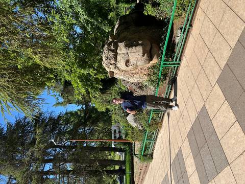 Traveller poses with a large stone lion sculpture in a leafy park.