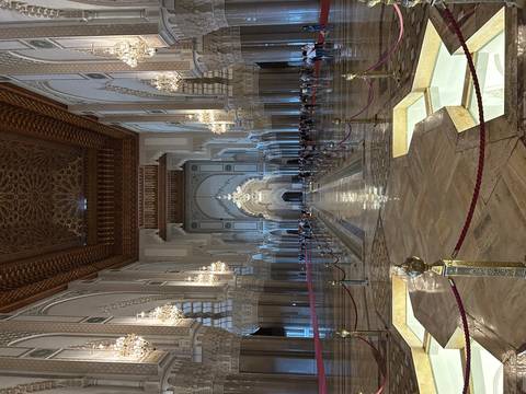 Grand interior hall of Hassan II Mosque adorned with chandeliers and intricate arches, visitors lining the nave.