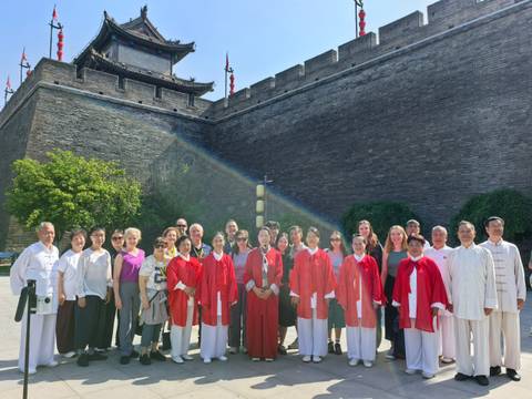 Tour participants stand in two rows beside Xi'an’s ancient city wall, a rainbow lens flare arching across the scene.