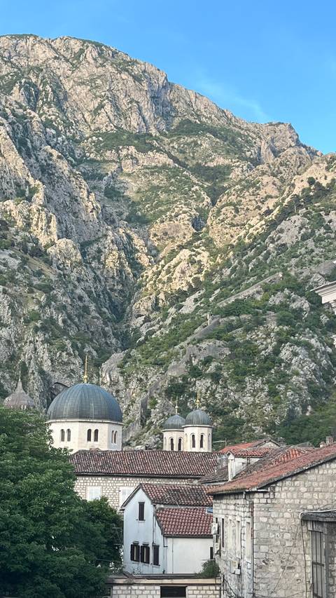 Steep rocky mountainside covered with sparse greenery rising above Kotor Bay area.