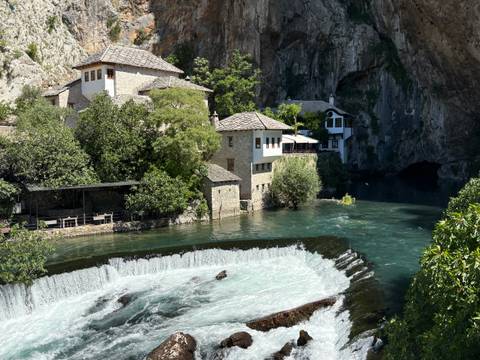 Historic Dervish monastery and stone houses beside turquoise river emerging from a cliff spring.