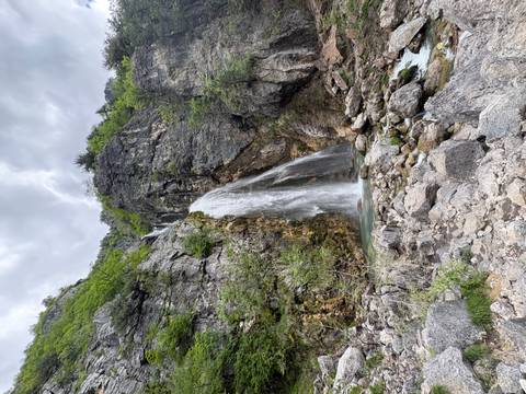 Tall waterfall cascading down rugged cliffs into a rocky pool in a mountain gorge.