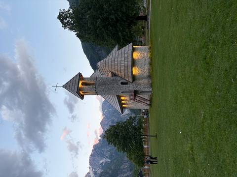 Stone Church of Theth lit warmly at dusk with mountain backdrop and grassy field.