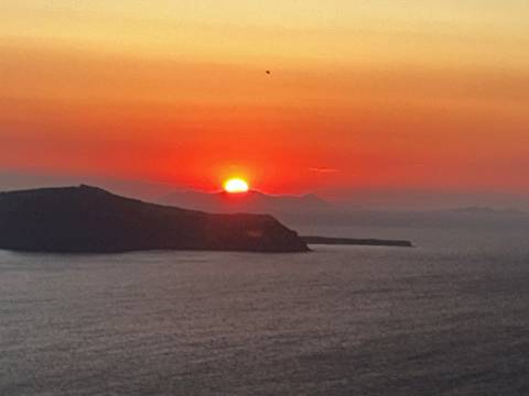 Fiery red sunset dipping behind a volcanic island in the Santorini caldera.