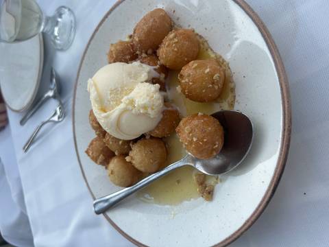 Plate of Greek loukoumades drizzled with honey, topped with vanilla ice cream.