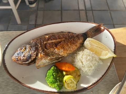 Grilled whole fish served with rice, lemon wedge and mixed vegetables on an oval plate.