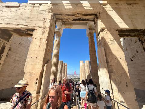 Grand marble columns and lintels of the Propylaea gateway on the Acropolis crowded with tourists.