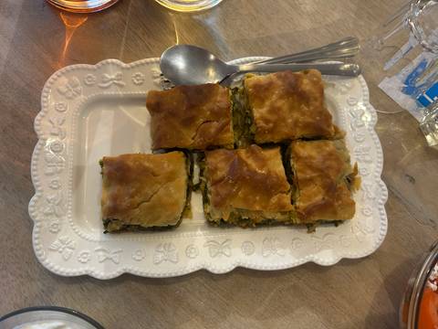 Tray of six pieces of Greek spanakopita with flaky golden crust served family-style.