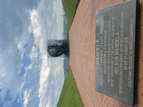Perspective view of the Nelson Mandela Capture Site sculpture composed of vertical steel poles lining a brick walkway.