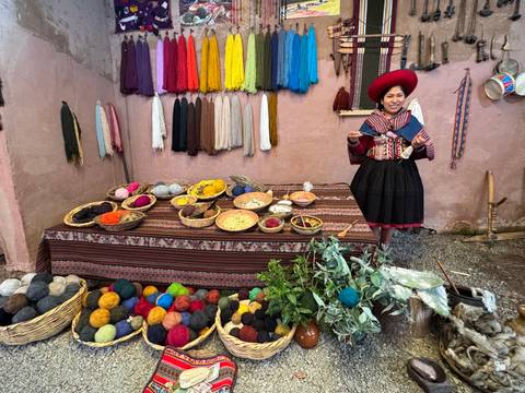 Andean woman in traditional dress demonstrating natural dyes and colourful yarns in a courtyard display.