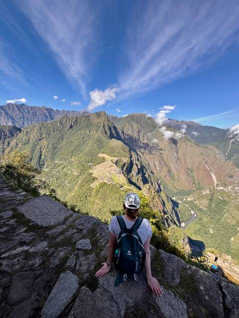 Traveller looking out over the terraces and steep green mountains of Machu Picchu from a high viewpoint.