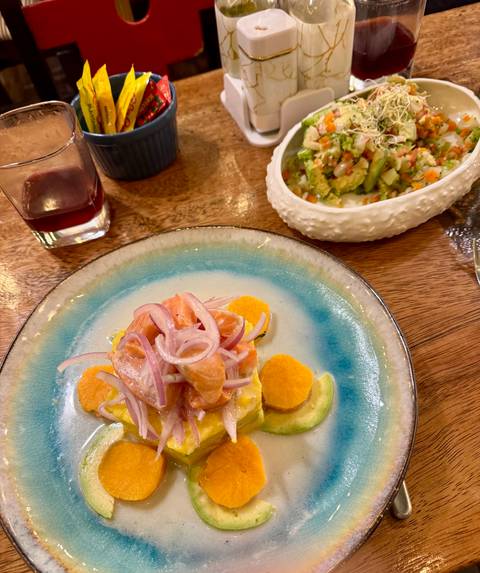 Close-up of a colourful Peruvian ceviche dish on a blue-rimmed plate with side salads on a wooden table.