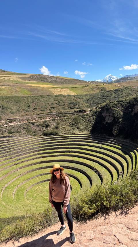 Concentric Inca agricultural terraces of Moray surrounded by green hills under bright sunlight.