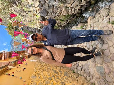 Two travellers smiling in a colourful cobblestone alley decorated with bright textiles and banners.