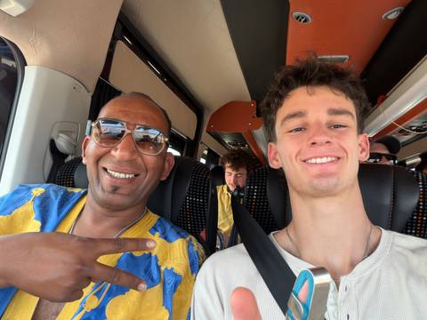 Smiling travellers taking a selfie inside a tour minibus, one making a peace sign.