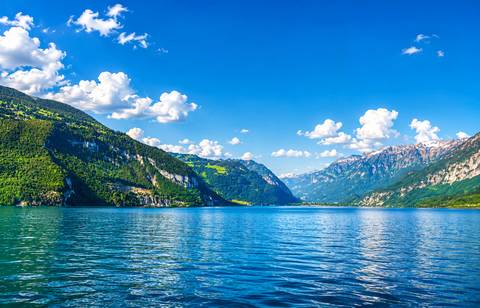 Crystal blue alpine lake with snow-capped mountains and scattered clouds.