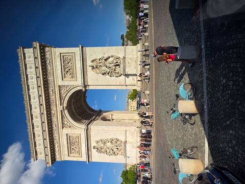 Crowds and cyclists gathered near the Arc de Triomphe on a sunny afternoon.